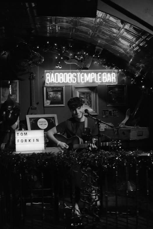 Tom Forkin playing guitar beside his letterboard sign at Bad Bobs, Temple Bar